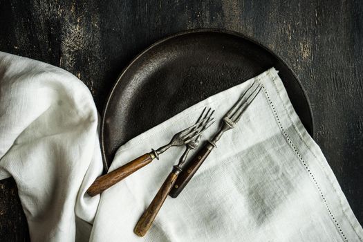 Rustic table setting ith vintage metal plate and cutlery on dark wooden table