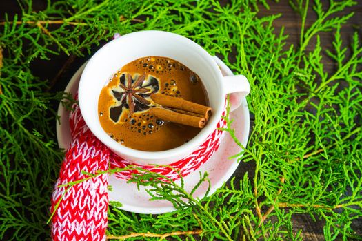 Mug of coffee with spices - cinnamon sticks and anise star with Christmas decor on dark wooden table with copyspace
