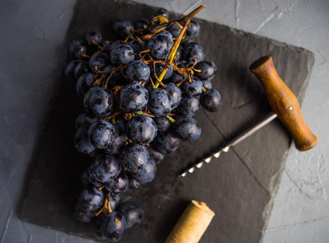 Organic ripe grape and vintage corkscrew on rustic background as a wine concept