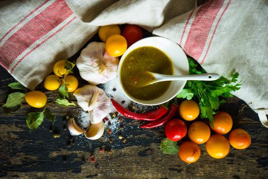 Traditional georgian sauce green tkemali with raw products on rustic wooden table