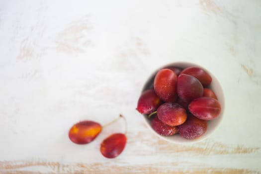 Organic plums in a bowl on white rustic table with copyspace