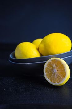 Fresh organic lemons in a bright yellow ceramic bowl on dark background