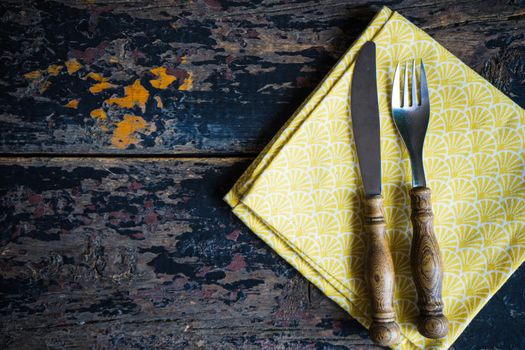 Rustic table setting with bright napkin nd silverware on dark wooden table