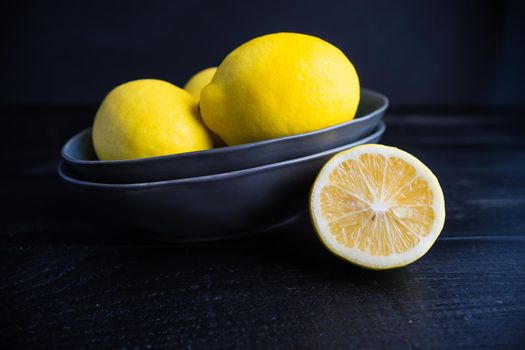 Fresh organic lemons in a bright yellow ceramic bowl on dark background