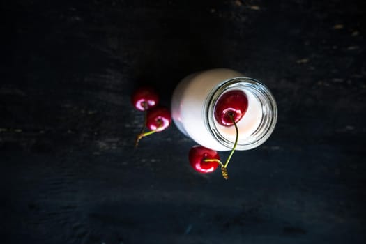 Bottle with yogurt and cherries on dark wooden table with copyspace
