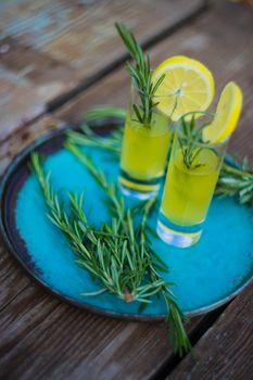 Traditional italian lemon alcohol drink limoncello with pieces of lemon and rosemary herb on dark wooden table