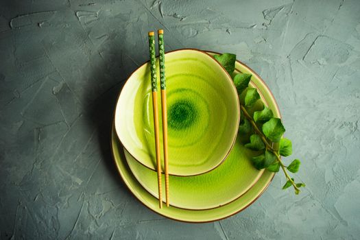 Rustic table setting with vintage ceramic plates, asian chopsticks and branch of ivy plant on dark old wooden table with copyspace