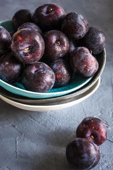 Fresh organic plums in a bowl on grey concrete background