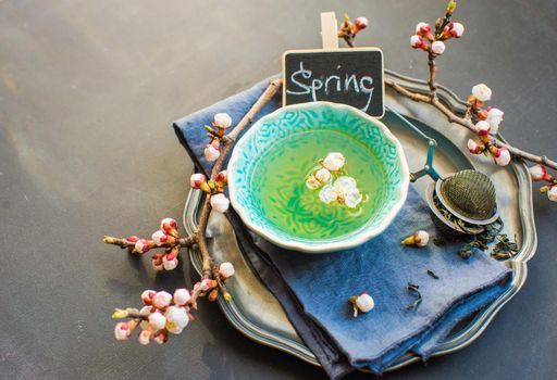Cup of green tea and peach blossom on dark rustic table as a spring time concept