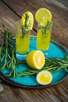 Traditional italian lemon alcohol drink limoncello with pieces of lemon and rosemary herb on dark wooden table