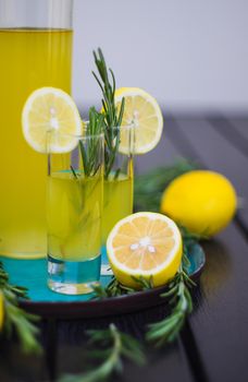 Traditional italian lemon alcohol drink limoncello with pieces of lemon and rosemary herb on dark wooden table