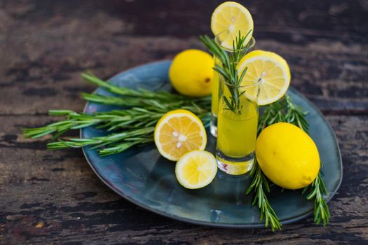 Traditional italian lemon alcohol drink limoncello with pieces of lemon and rosemary herb on dark wooden table