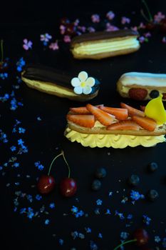 Different eclair dessert on dark wooden table decorated with strawberries and flowers