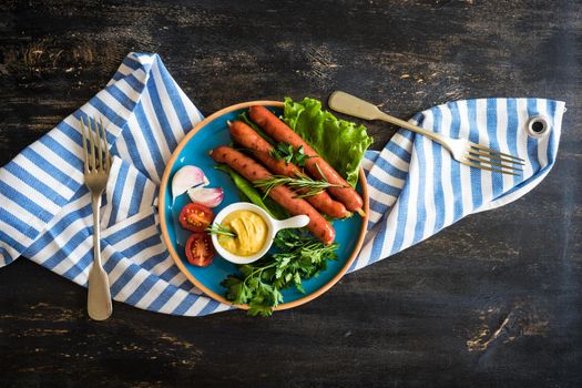 Unhealthy food - grilled sausages with rosemary and tomatoes on dark wooden table