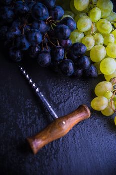 Organic ripe grape and vintage corkscrew on rustic background as a wine concept