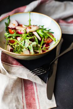 Spring healthy salald with fresh organic tomatoes, radish and rukkola herb on rustic plate with napkin and silverware