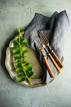 Rustic table setting with vintage ceramic plates and branch of ivy plant on dark old wooden table with copyspace