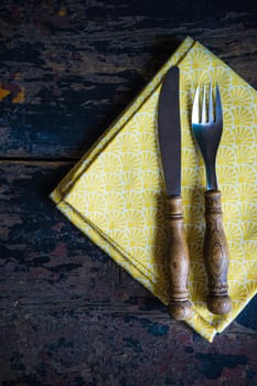 Rustic table setting with bright napkin nd silverware on dark wooden table