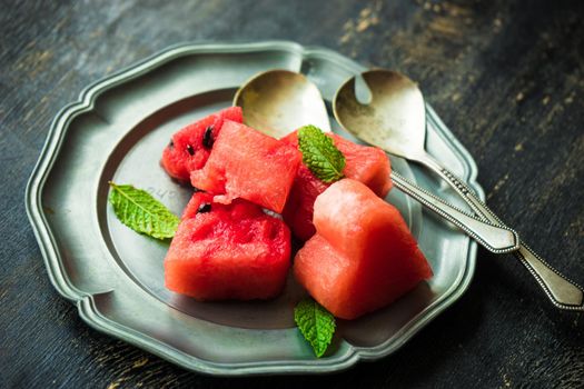 Organic sweet watermelon heart shaped pieces on vntage plate decorated with mint on rustic wooden table with copyspace