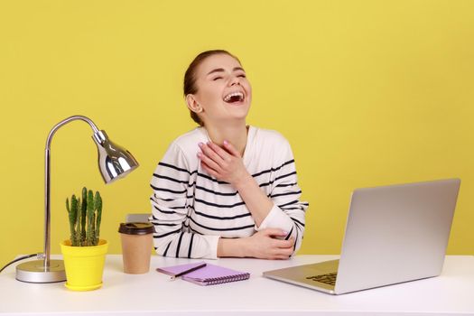 Amused happy woman employee laughing out loud, being hysterical at crazy joke on laptop, having break at workplace home office. Indoor studio studio shot isolated on yellow background.