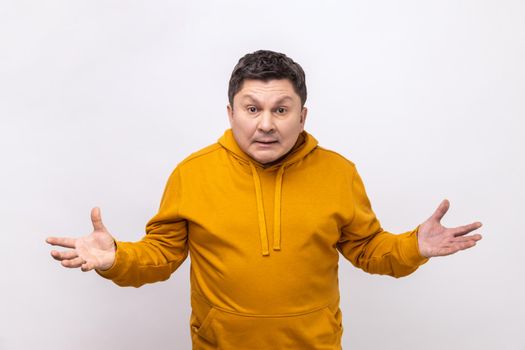 Portrait of angry confused man standing with raised hands and surprised indignant expression, asking why how, what reason, wearing urban style hoodie. Indoor studio shot isolated on white background.