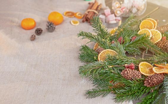 Rustic Christmas table with natural spruce wreath, dried oranges, fresh tangerines, pine cones on a fabric tablecloth. Copy space