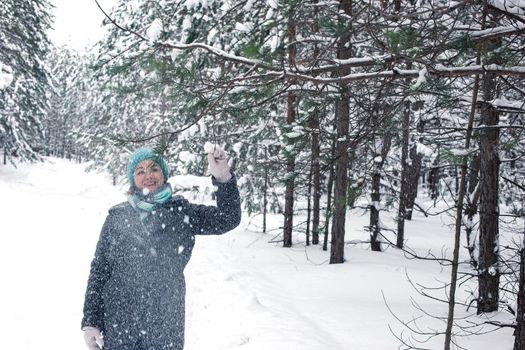 A happy woman in a winter snow-covered forest, holding a pine branch, shaking off the snow. Walk with winter forest.