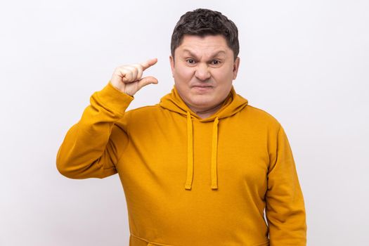 Portrait of funny man making little bit gesture with fingers and smiling sarcastic, showing minimum size, begging few more, wearing urban style hoodie. Indoor studio shot isolated on white background.