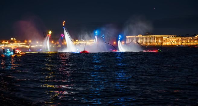 A lot of flyboarders and brightly dressed up jet skiers perform their show at a holiday in the center of St. Petersburg at night, water activities. High quality photo