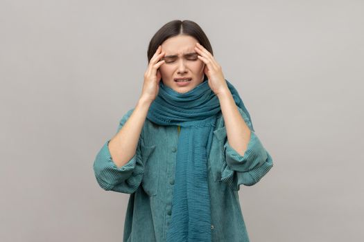 Upset frustrated woman standing wrapped in scarf, feeling headache, cold symptoms, runny nose, frowning face, wearing casual style jacket. Indoor studio shot isolated on gray background.