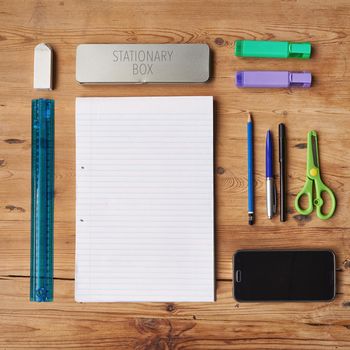 School supplies, stationary or equipment for young working and studying students top view. Assortment, variety or array of education essentials items including a phone and notebook on a wooden desk.