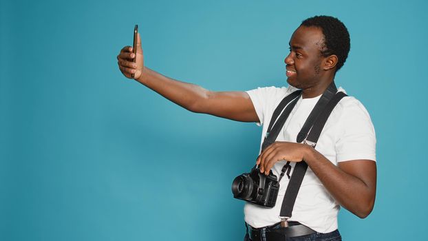 Photographer taking pictures using smartphone in studio, holding professional camera to pose. Capturing images with dslr lens and photography equipment, leisure fun activity. Focused view.
