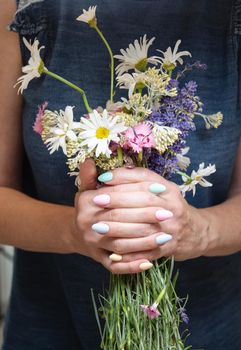 a young woman with a beautiful summer manicure holds a bouquet of wild flowers in pastel shades. High quality photo