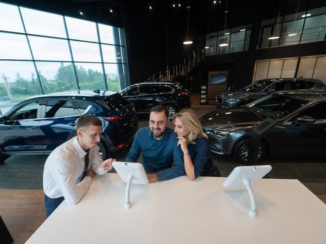 Caucasian married couple chooses a car in a car dealership on digital tablets