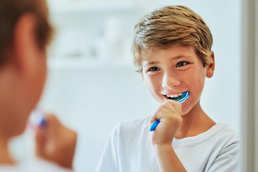 Got to brush those teeth in the morning. a cheerful young boy looking at his reflection in a mirror while brushing his teeth in the bathroom at home during the day