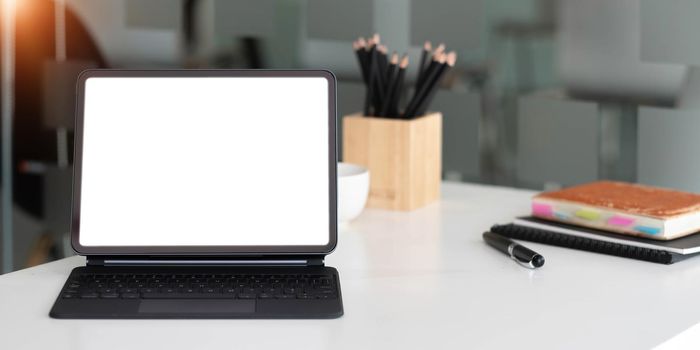 Mockup blank screen tablet with magic keyboard on wooden table in office..