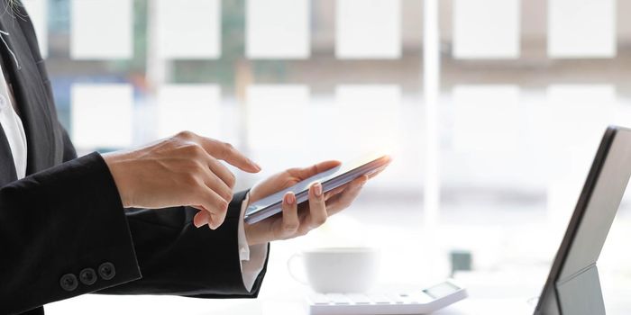 Closeup woman hands using smartphone while sitting at her office desk in modern room..