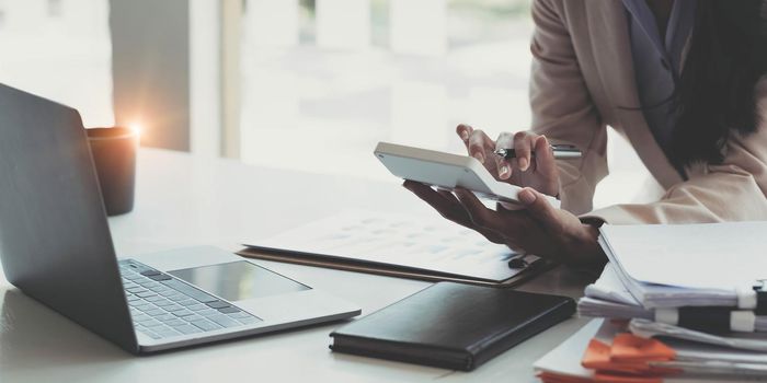 Close up Businessman using calculator and laptop for calaulating finance, tax, accounting, statistics and analytic research concept.