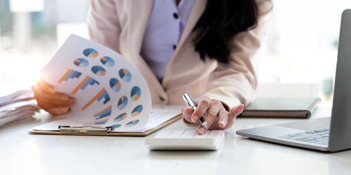 Close up Business woman using calculator and laptop for do math finance on wooden desk in office and business working background, tax, accounting, statistics and analytic research concept.