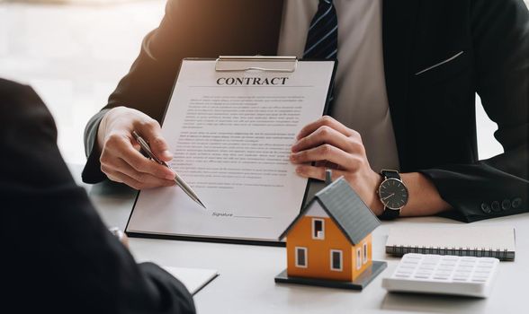 Real estate broker agent presenting and consult to customer to decision making sign insurance form agreement, buy and sell home model, concerning mortgage loan offer for and house insurance.