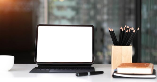 Mockup blank screen tablet with magic keyboard on wooden table in office..