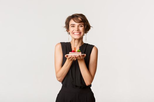 Happy beautiful b-day girl holding birthday cake and smiling, standing over white background.