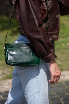 close-up photo of small green leather bag in a woman hands. outdoors photo. Girl in a brown shirt and blue jeans