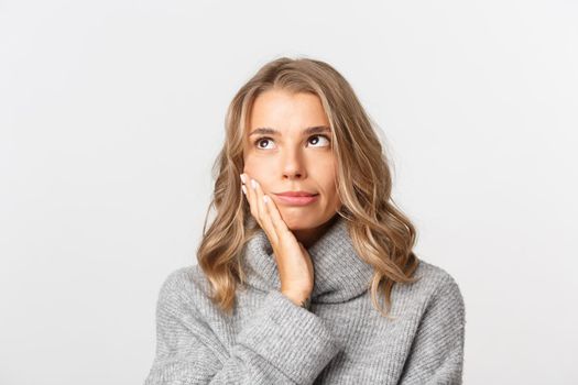 Close-up of annoyed blond woman in grey sweater, roll her eyes and slap face irritated with something, standing over white background.