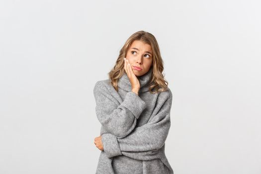 Image of sad thoughtful girl looking at upper left corner nostalgic, standing over white background in grey casual sweater.