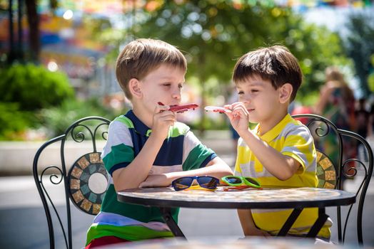 Two little kid boys waiting on table for healthy breakfast in hotel restaurant or city cafe. Child sit on comfortable chair play with toy aircraft, relaxed, enjoy their vacation. Summer holiday with children concept.