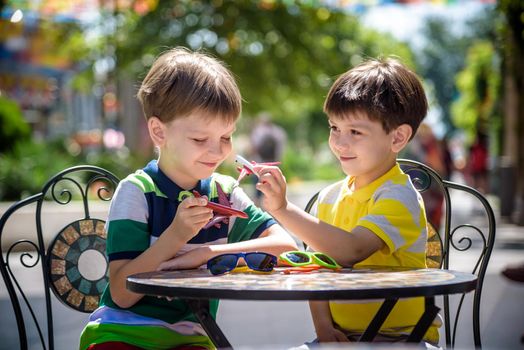 Two little kid boys waiting on table for healthy breakfast in hotel restaurant or city cafe. Child sit on comfortable chair play with toy aircraft, relaxed, enjoy their vacation. Summer holiday with children concept.