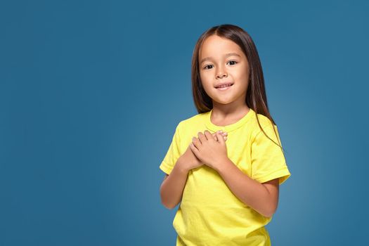 little girl in yellow t-shirt hands on her heart on the blue background