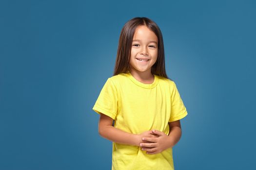 Little girl in yellow t-shirt is smiling on blue background