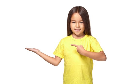 Little girl in yellow t-shirt holding her hand out and showing copy space for your product isolated on white background
